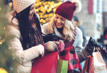Two women hold holiday shopping bags and laugh