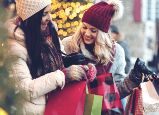 Two women hold holiday shopping bags and laugh