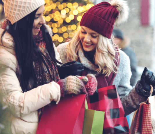 Two women hold holiday shopping bags and laugh