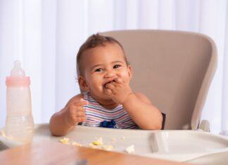 Cute baby child eating food, sitting on high chair.