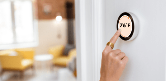 Woman adjusts home thermostat to 76 degrees farenheit